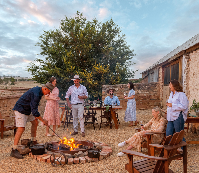 Friends gathered for dinner around an open fire in a backyard