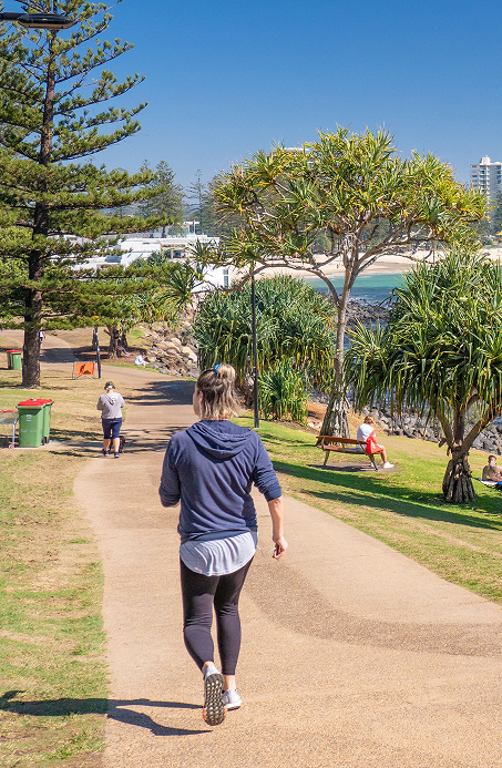 Person walking outdoors, green trees and water scenery in the background