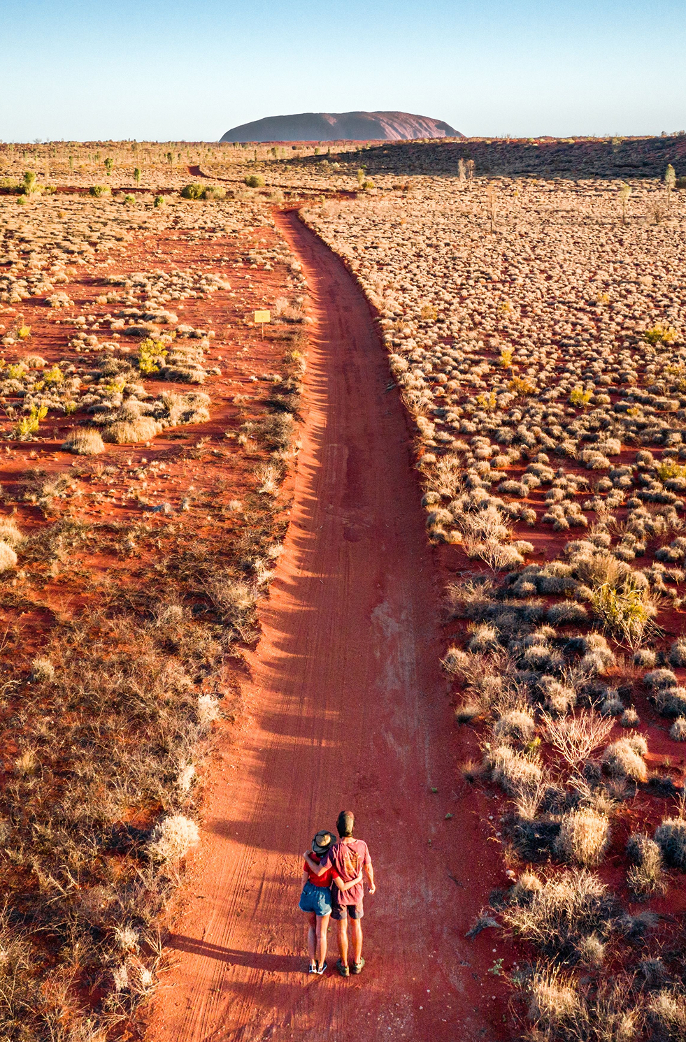 Aerial view of couple standing on a dirt road lookout facing the desert at Uluru-Kata Tjuta National Park