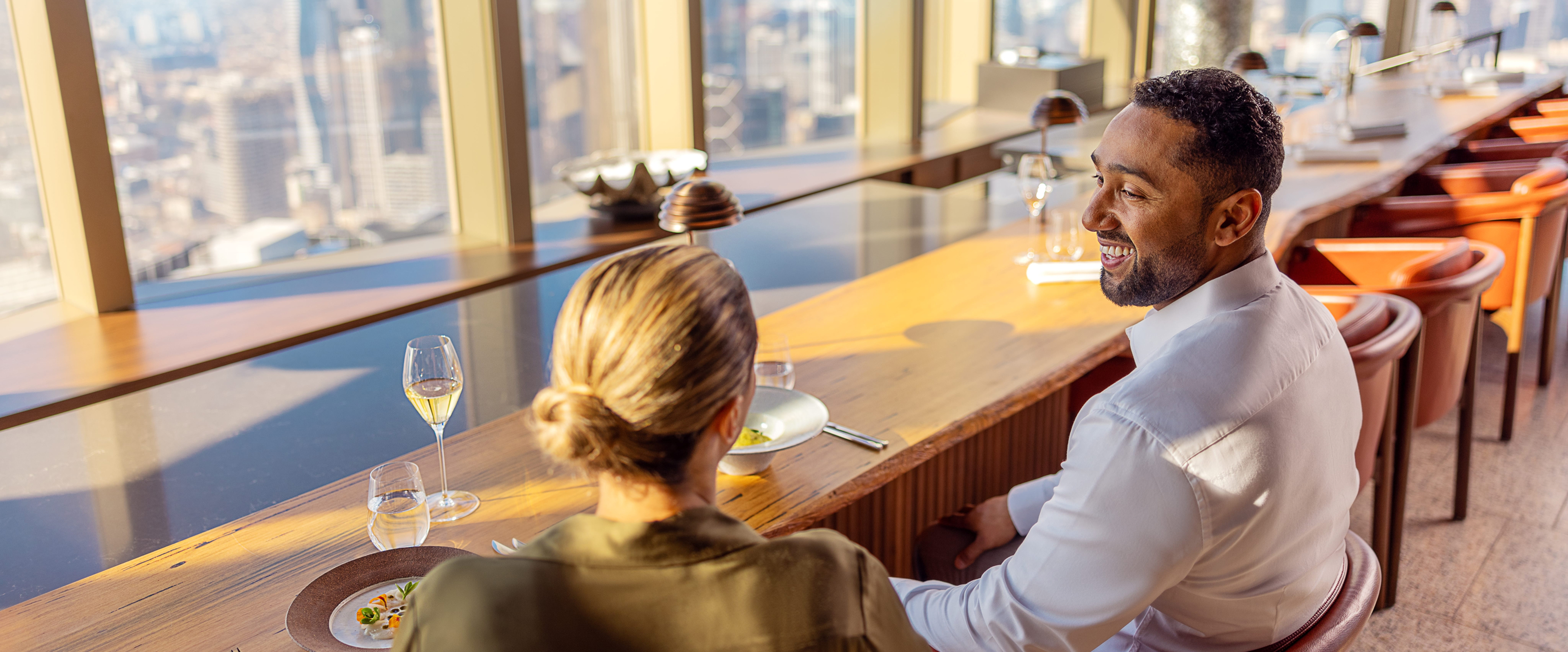 Two professionals enjoying fine dining in a high-rise restaurant overlooking a scenic city view