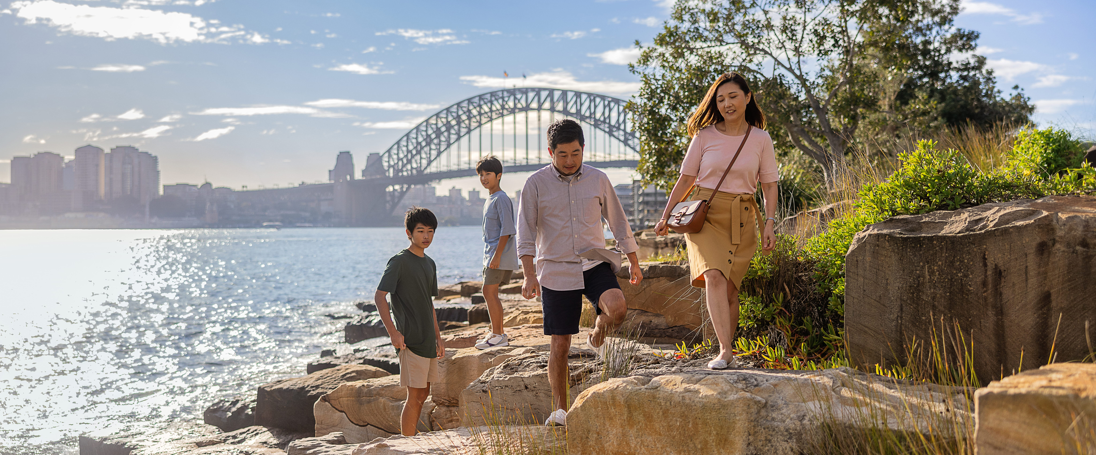 Young family exploring rocks at Barangaroo Reserve with Sydney Harbour Bridge in the background
