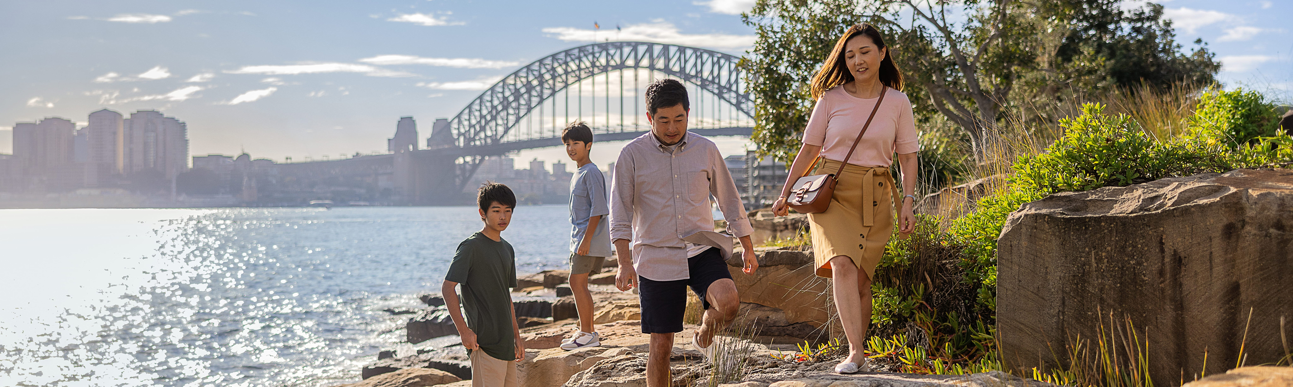 Young family exploring rocks at Barangaroo Reserve with Sydney Harbour Bridge in the background