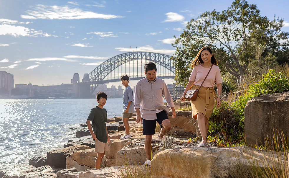 Young family exploring rocks at Barangaroo Reserve with Sydney Harbour Bridge in the background