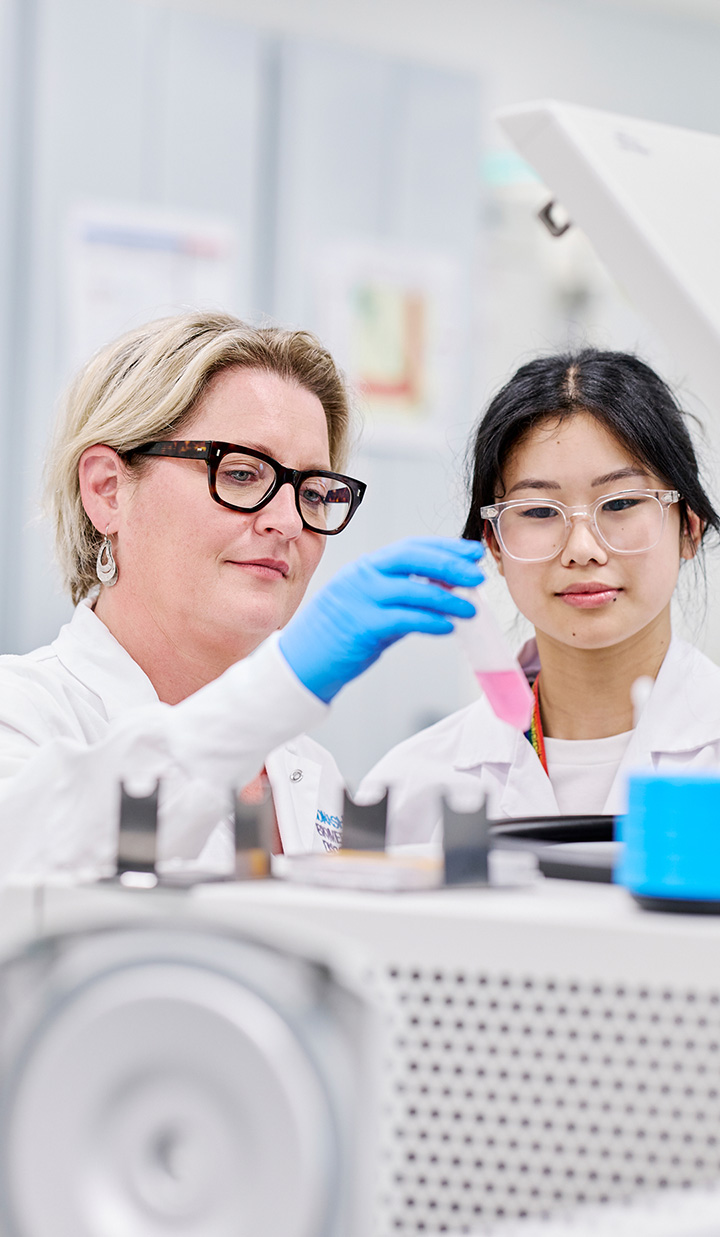 Two women checking a sample inside a piece of machinery.