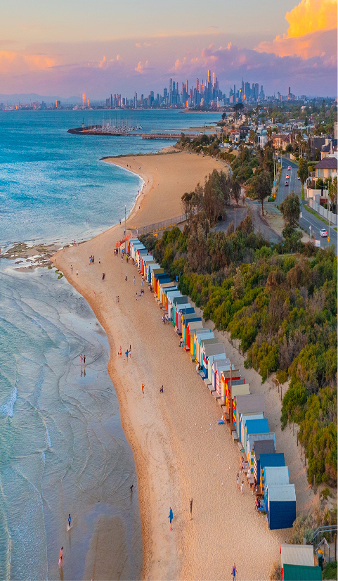 Aerial view of Brighton Beach in Melbourne with colourful bathing boxes and city skyline in the distance