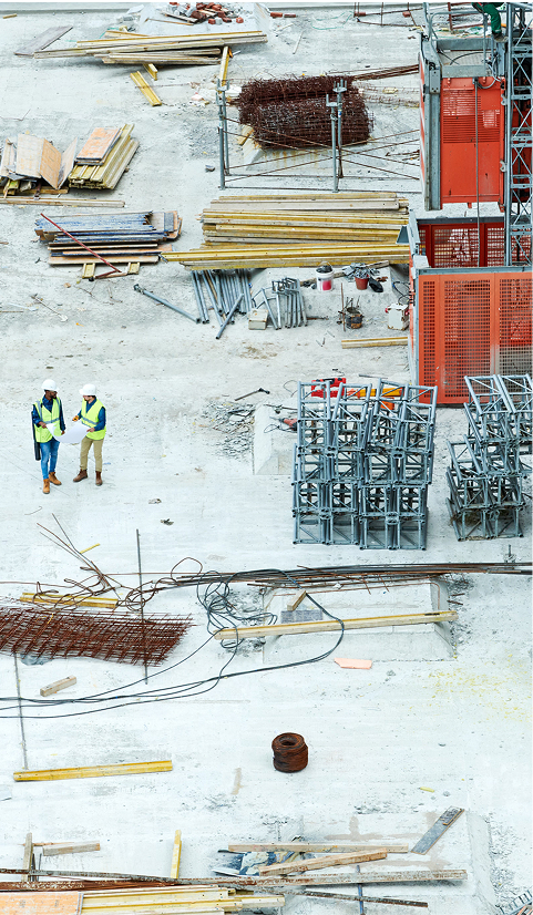 Aerial view of a construction site with materials, scaffolding and two workers in high-visibility vests walking across the slab.jpg