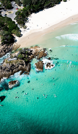 Aerial view of a sandy beach with turquoise water, rocky outcrops, and swimmers in the ocean