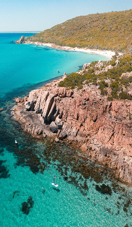 Aerial view of rugged coastal cliffs and crystal-clear blue water with people paddle-boarding in Noosa