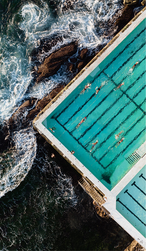 Aerial view of swimmers in an ocean pool beside waves crashing against the rocks, Bondi, Australia