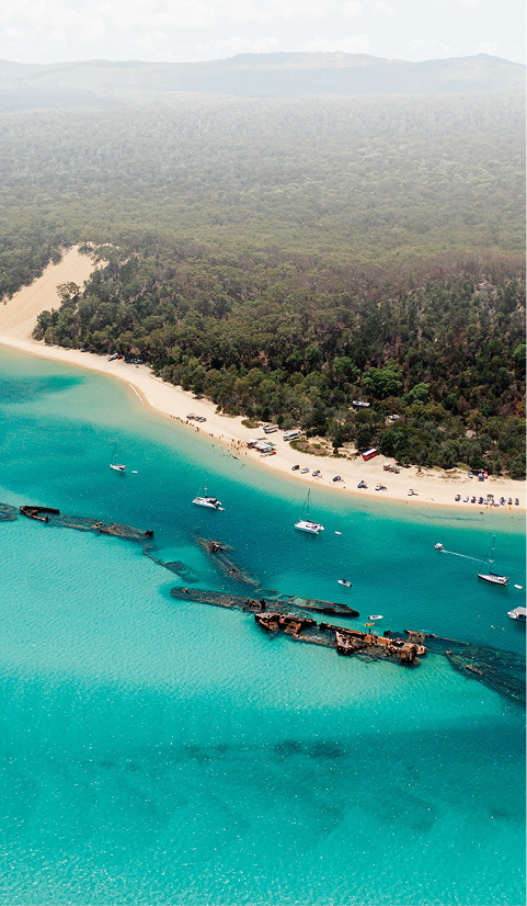 Aerial view of the Tangalooma Wrecks and turquoise water off Moreton Island with boats anchored near the beach