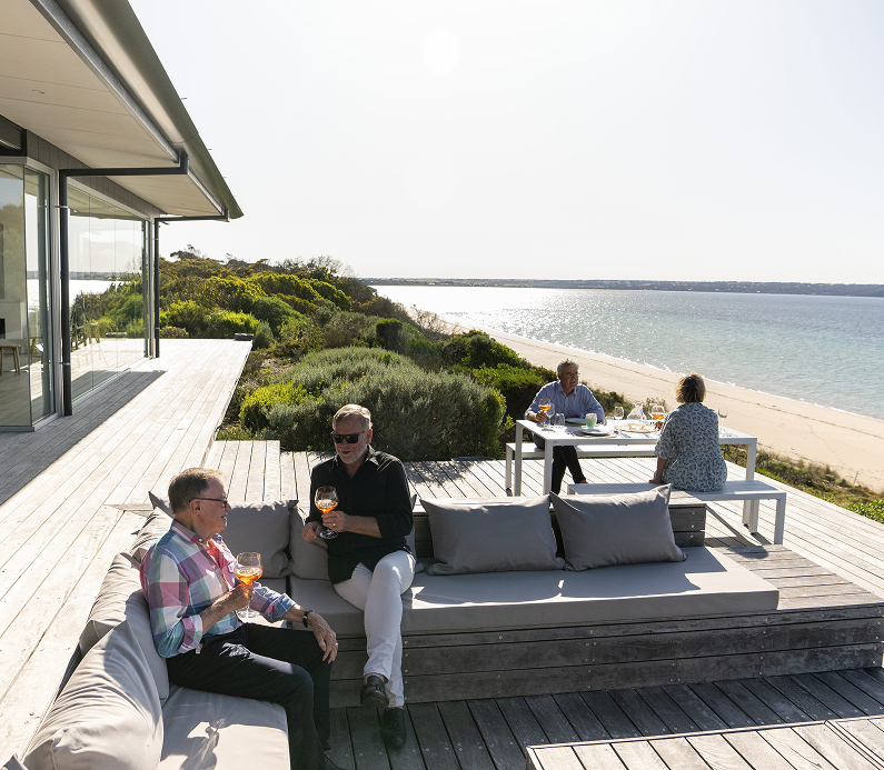 Coastal home with people enjoying the deck and views of the scenic beachfront.