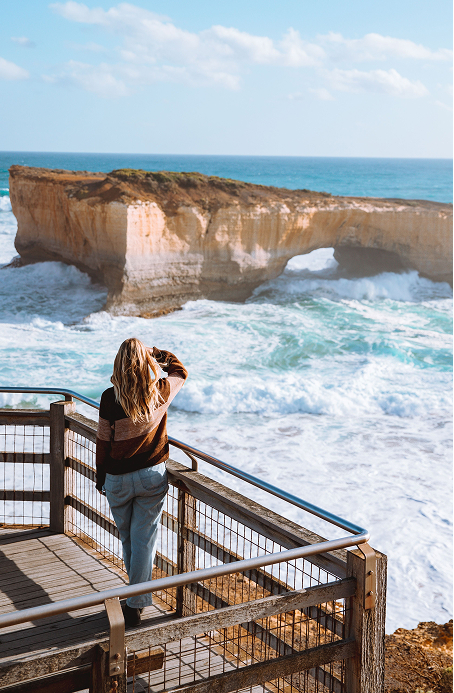 Person overlooking The Bakers Oven rock arch and ocean waves on the Great Ocean Road on a sunny day