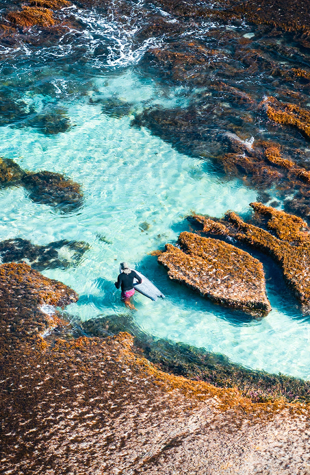 Surfer holding a board, walking over wet rocks at Surfers Point, Margaret River.