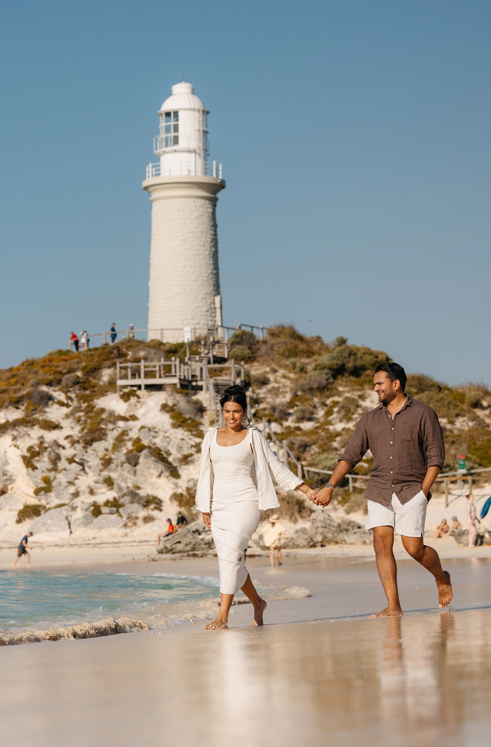 Couple walking on Pinky_s Beach, Rottnest Island, lighthouse and white sand dunes in the background.