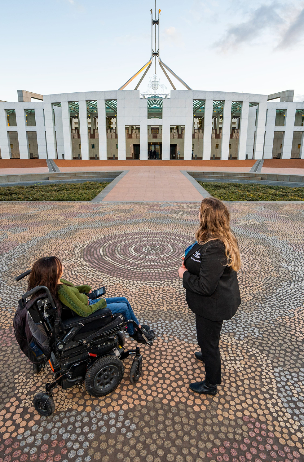Person in a wheelchair and companion on Indigenous mosaic at Parliament House forecourt, Canberra.