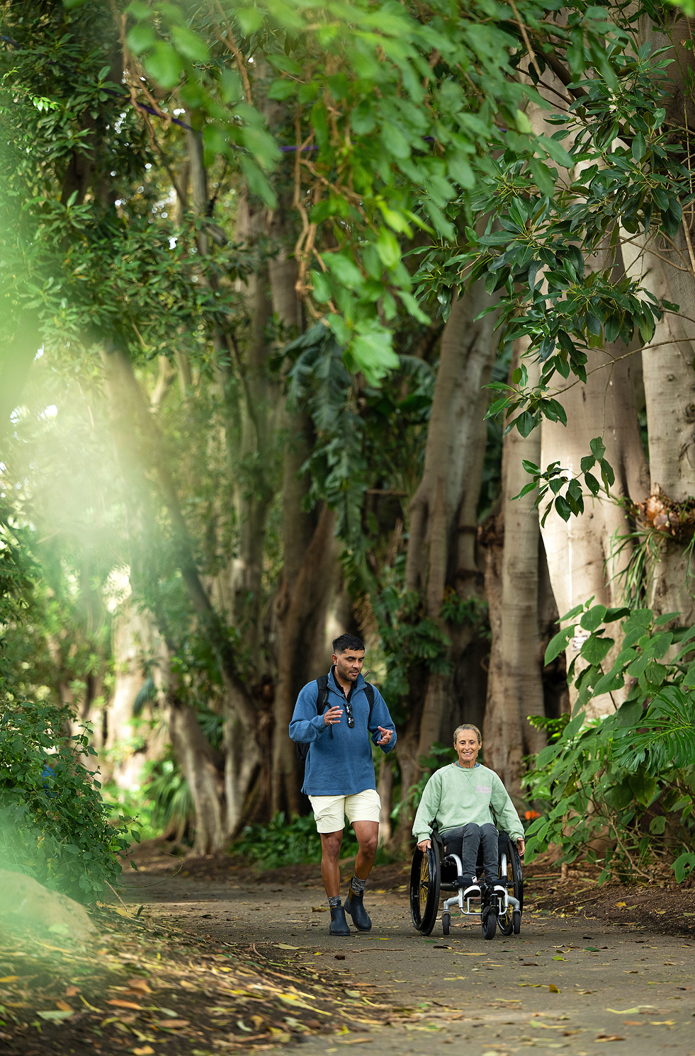 Person in wheelchair and companion exploring lush, accessible path at Adelaide Botanic Gardens.