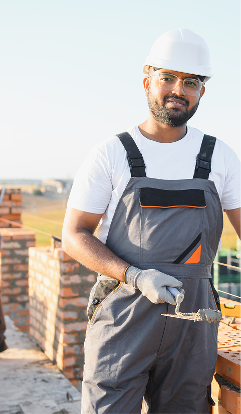 Bricklayer in safety gear holding a trowel while working on a brick wall at an outdoor construction site