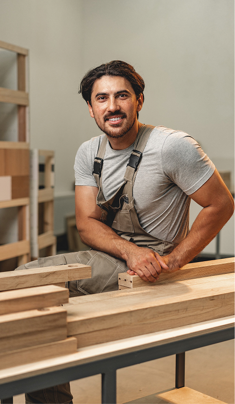 Carpenter smiling while working with timber pieces in a workshop