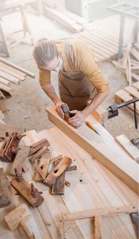 Carpenter working on timber in a workshop surrounded by woodworking tools
