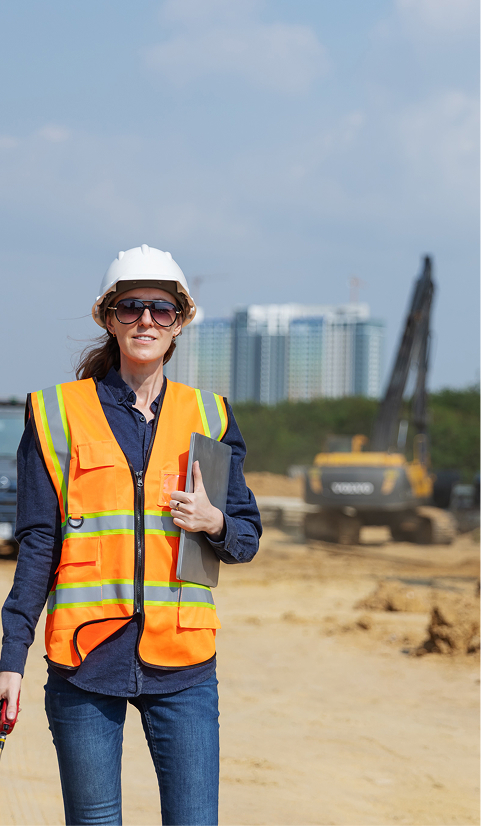 Construction site supervisor wearing a hard hat and high-visibility vest, standing in front of machinery