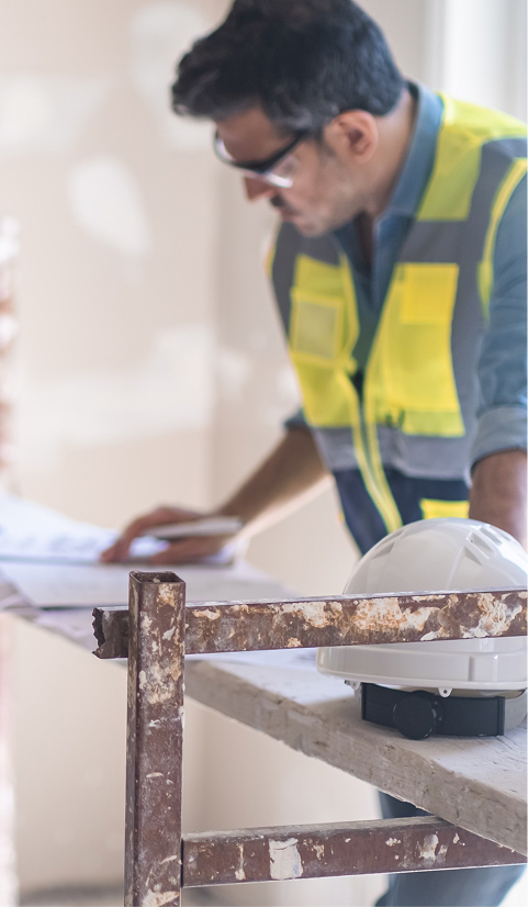 Construction supervisor wearing safety glasses and a high-visibility vest reviewing building plans on a workbench