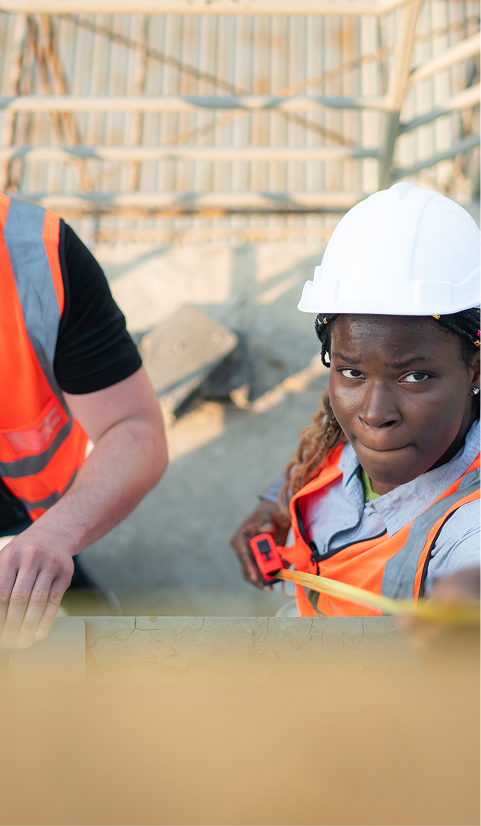 Construction worker in a hard hat and safety vest using a tape measure at a building site