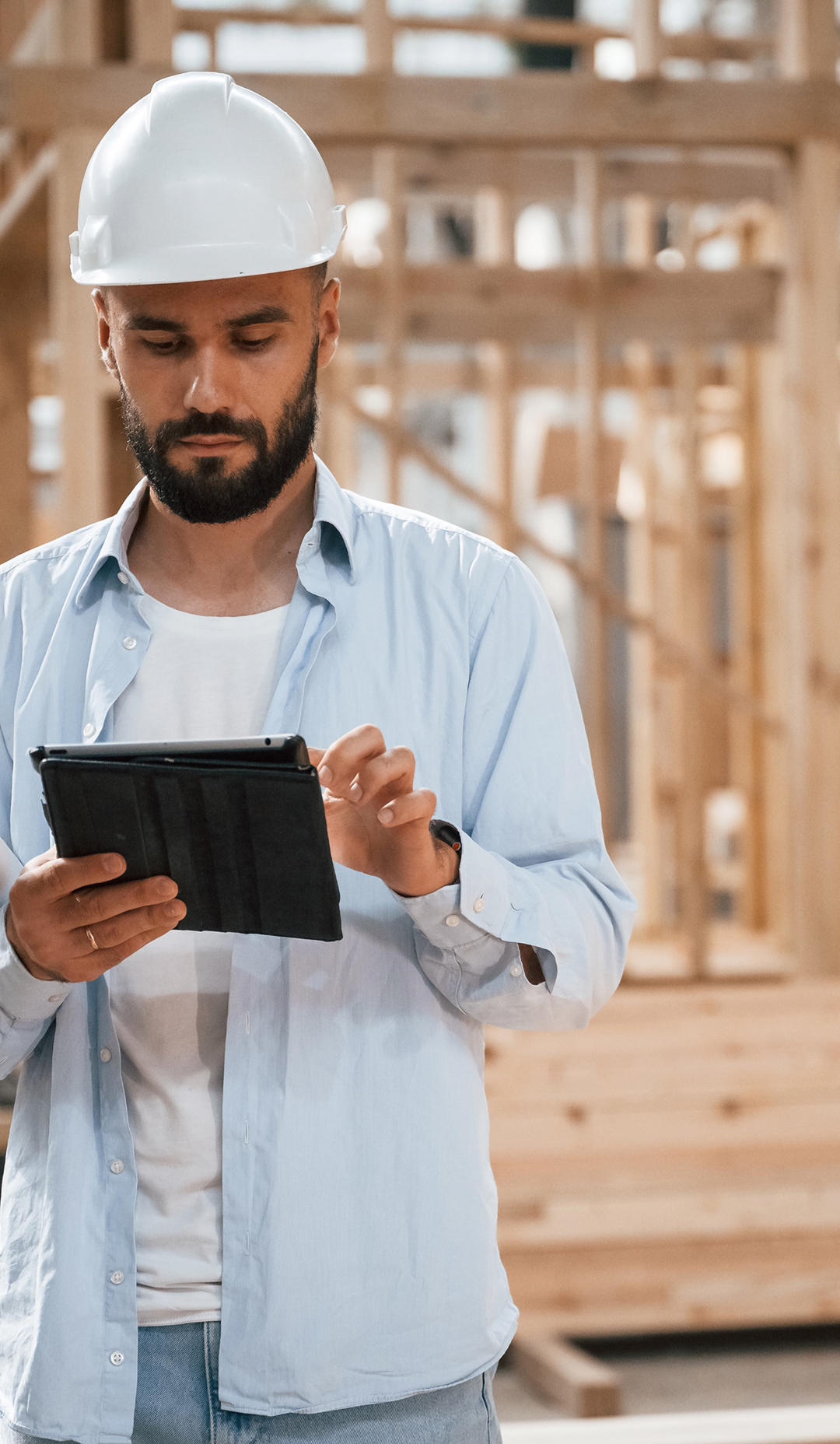 Construction worker in a hard hat using a digital tablet inside a timber-frame building