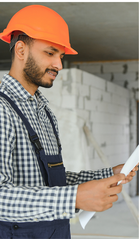 Construction worker wearing an orange hard hat reviewing building plans indoors