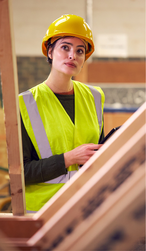 Female construction inspector in a hard hat and safety vest examining timber framing inside a build