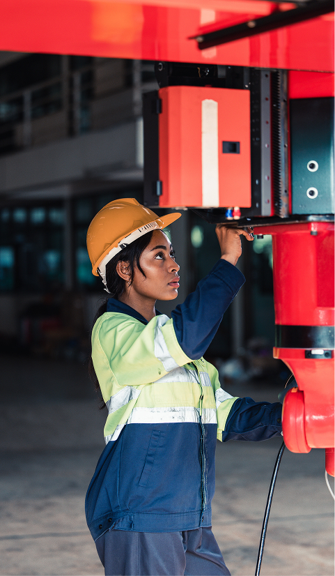 Female technician in a hard hat and reflective jacket operating industrial machinery indoors