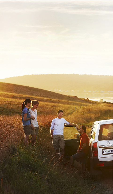 Group of friends standing beside a 4WD vehicle at sunset on a grassy hillside