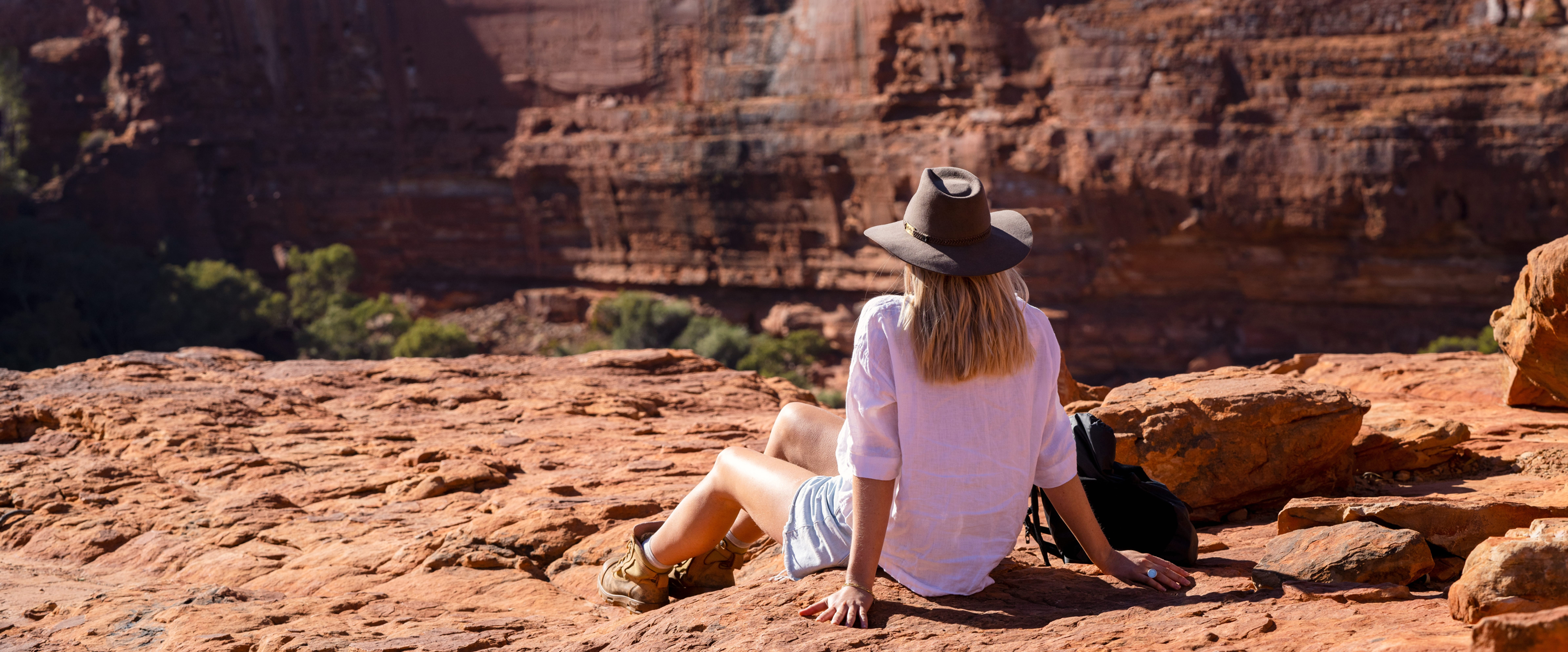 Female hiker seated on rocks, gazing at canyon view in Watarrka National Park