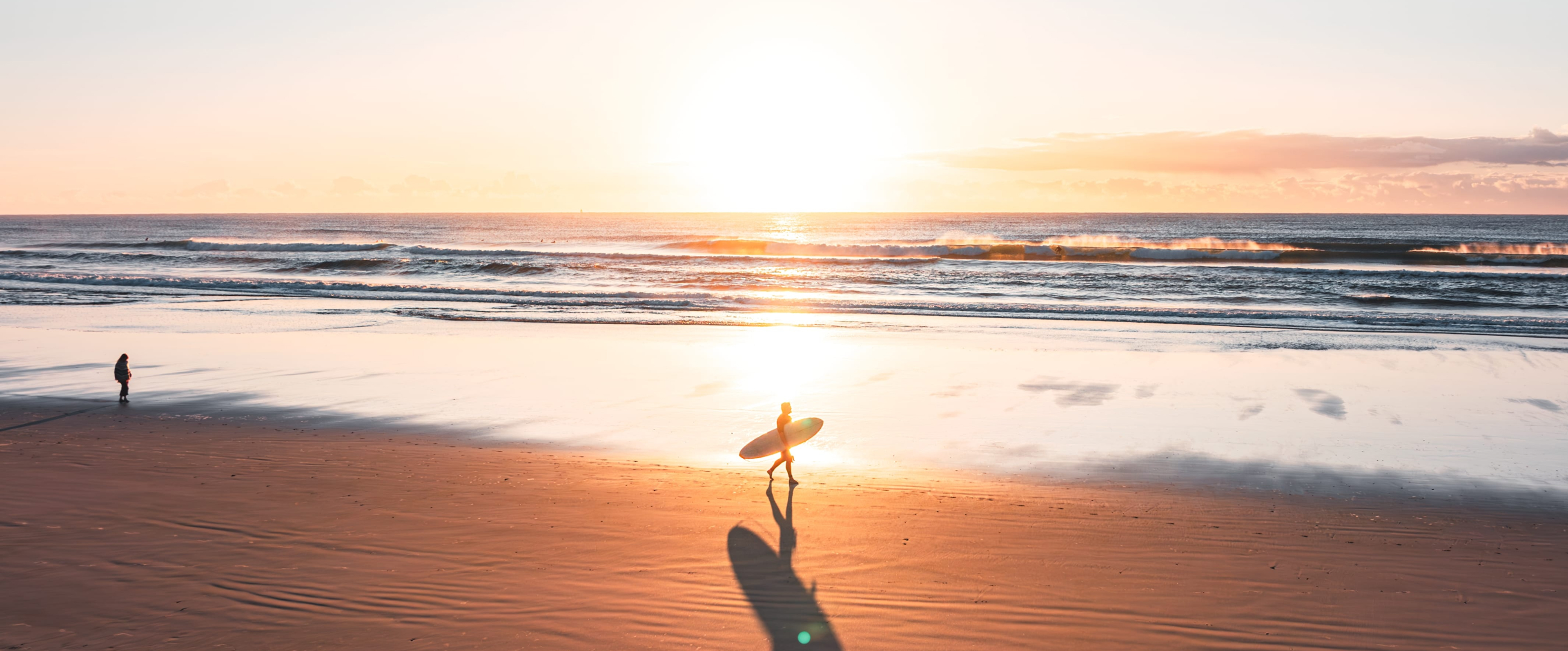 Surfer silhouetted at sunrise on Broken Head beach, NSW, with golden light and gentle waves
