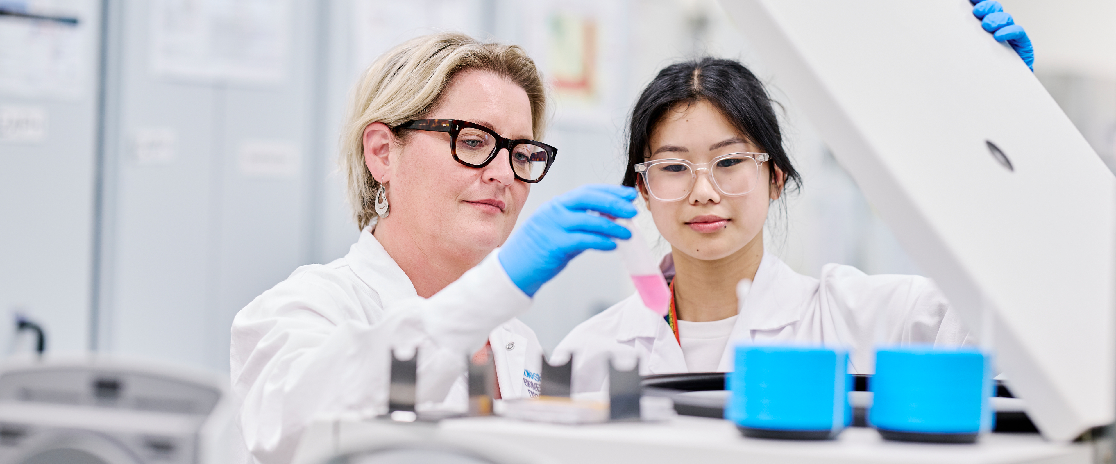 Two scientists in lab coats examine a sample in a centrifuge in a laboratory