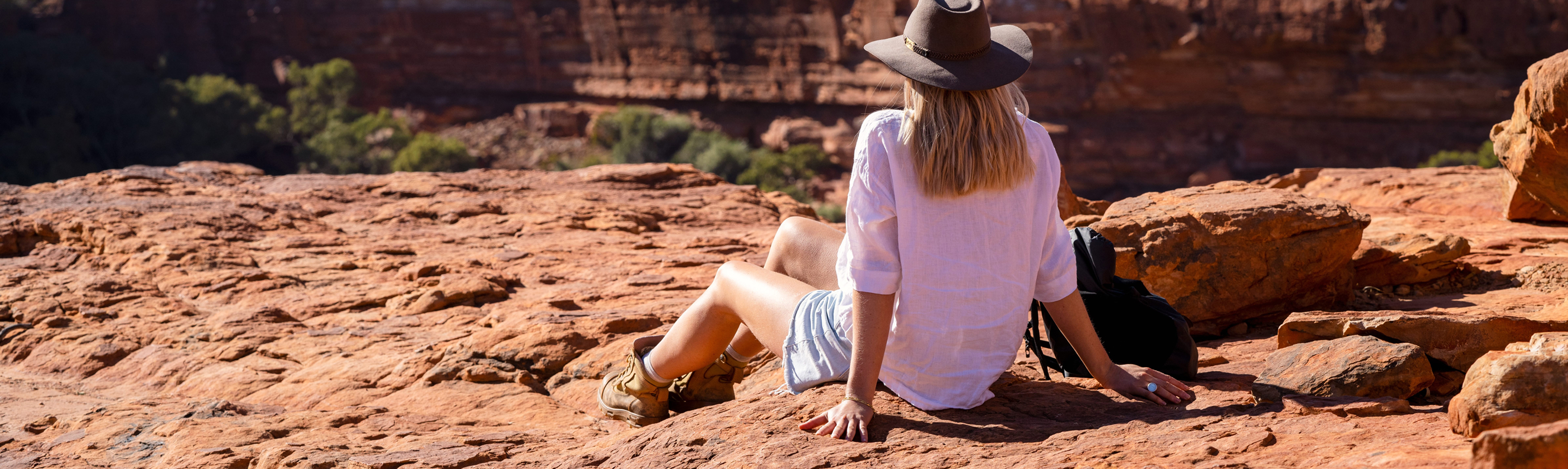 Female hiker seated on rocks, gazing at canyon view in Watarrka National Park