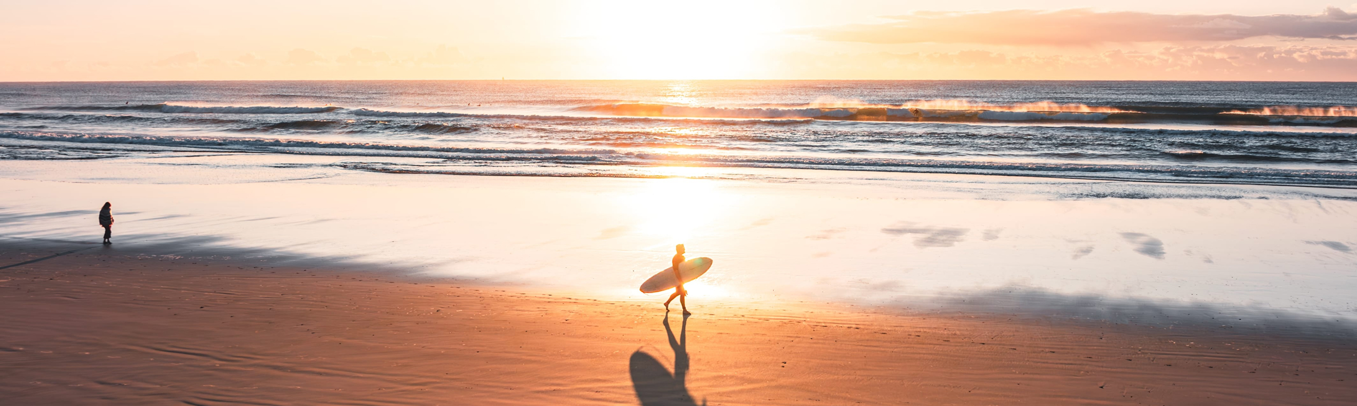Surfer silhouetted at sunrise on Broken Head beach, NSW, with golden light and gentle waves