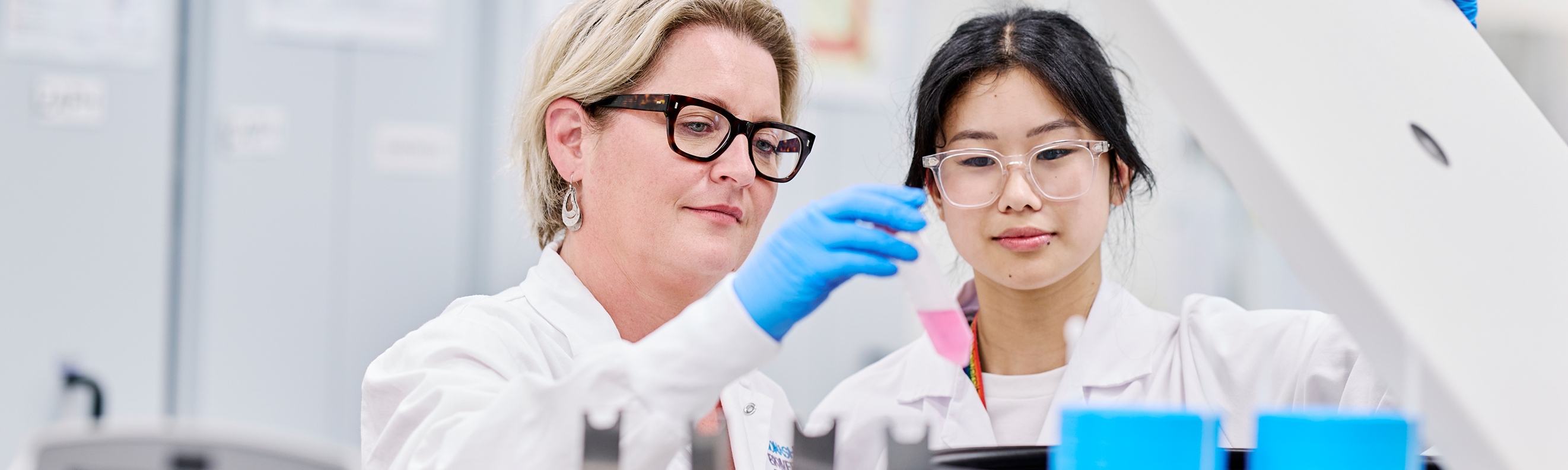 Two scientists in lab coats examine a sample in a centrifuge in a laboratory