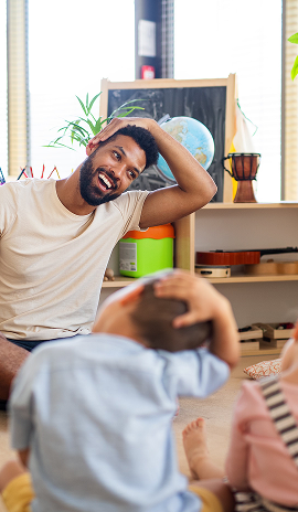 Male educator sitting on the floor with young children, leading an interactive classroom activity