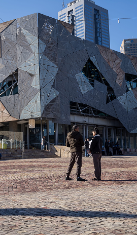 People standing in Federation Square with its modern geometric architecture and city buildings behind