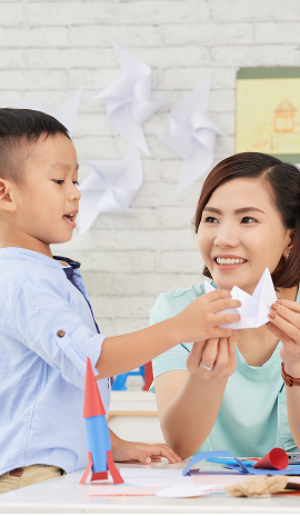 Teacher helping a young child fold a paper craft during a classroom activity