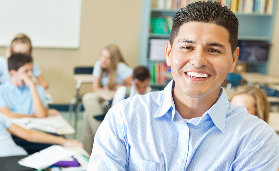 Teacher in sharp focus, standing with students working at desks behind