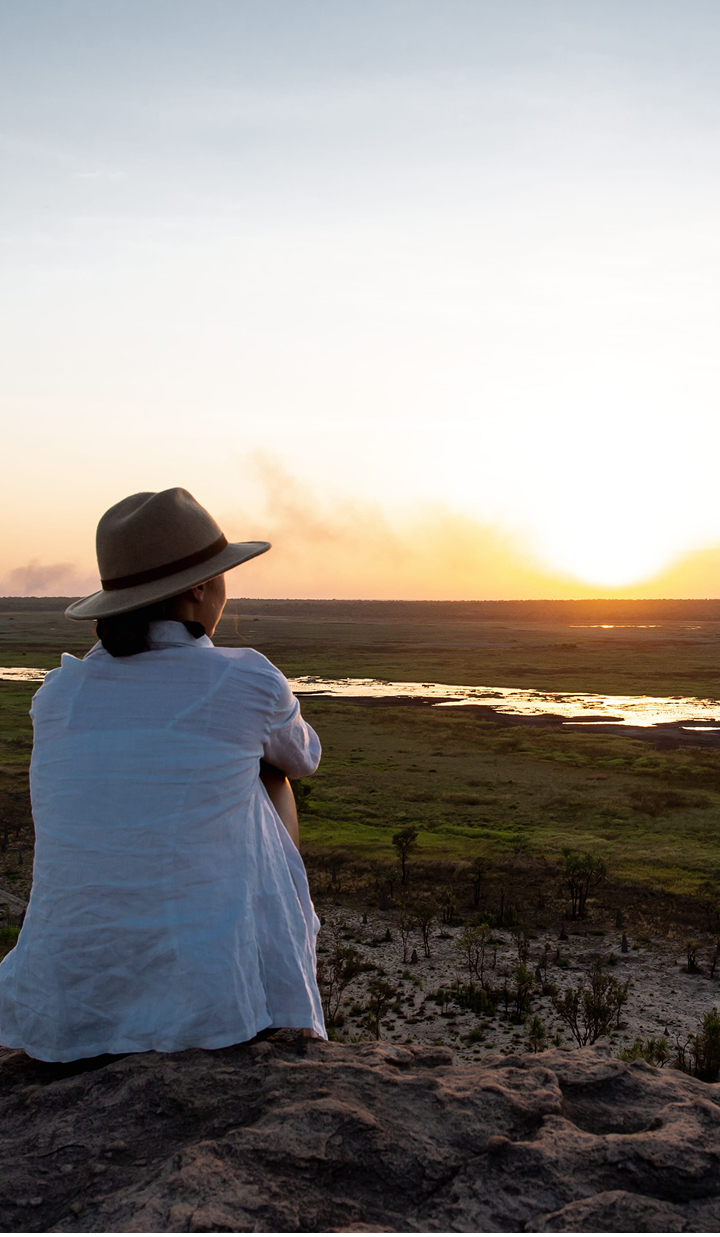 Woman in a hat watching a sunset over a grassy plain