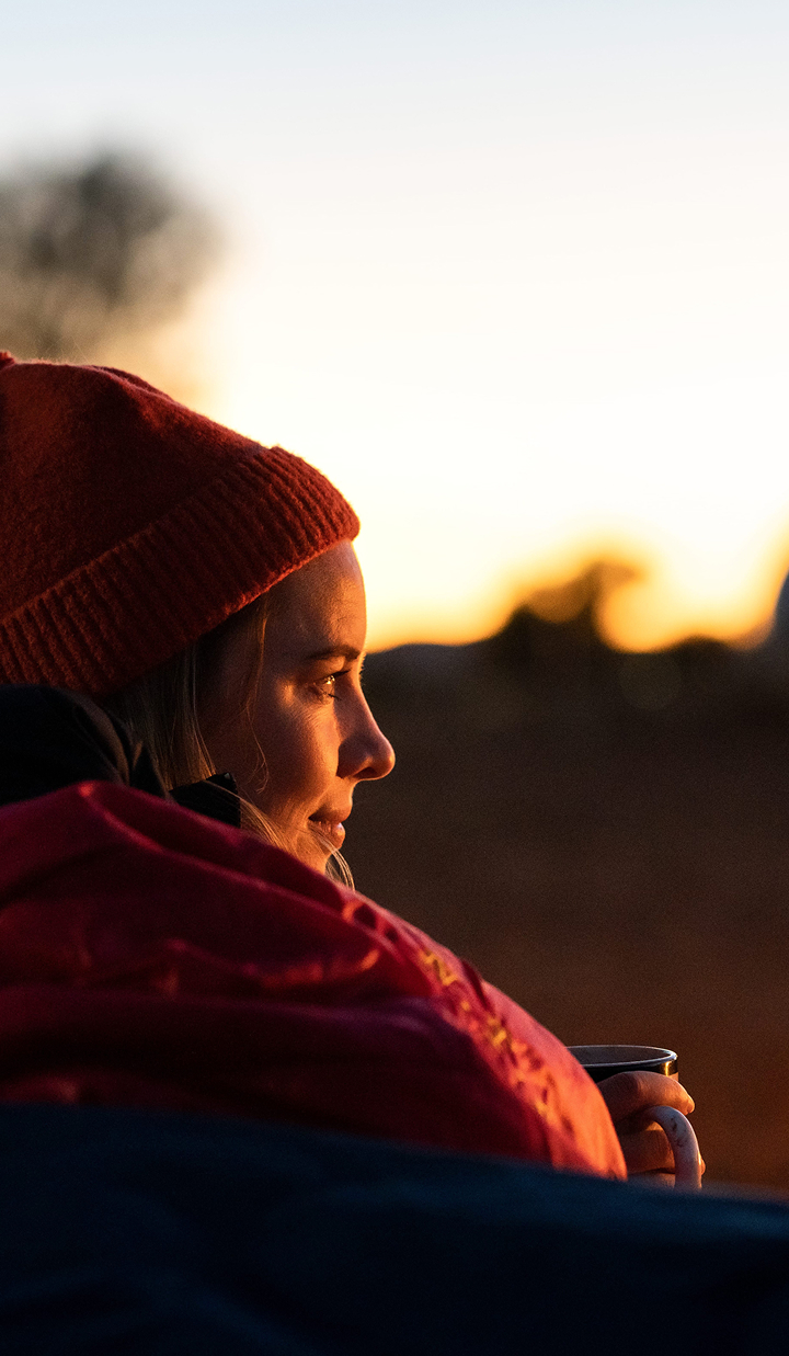Woman in a hat watching a sunset with a mug