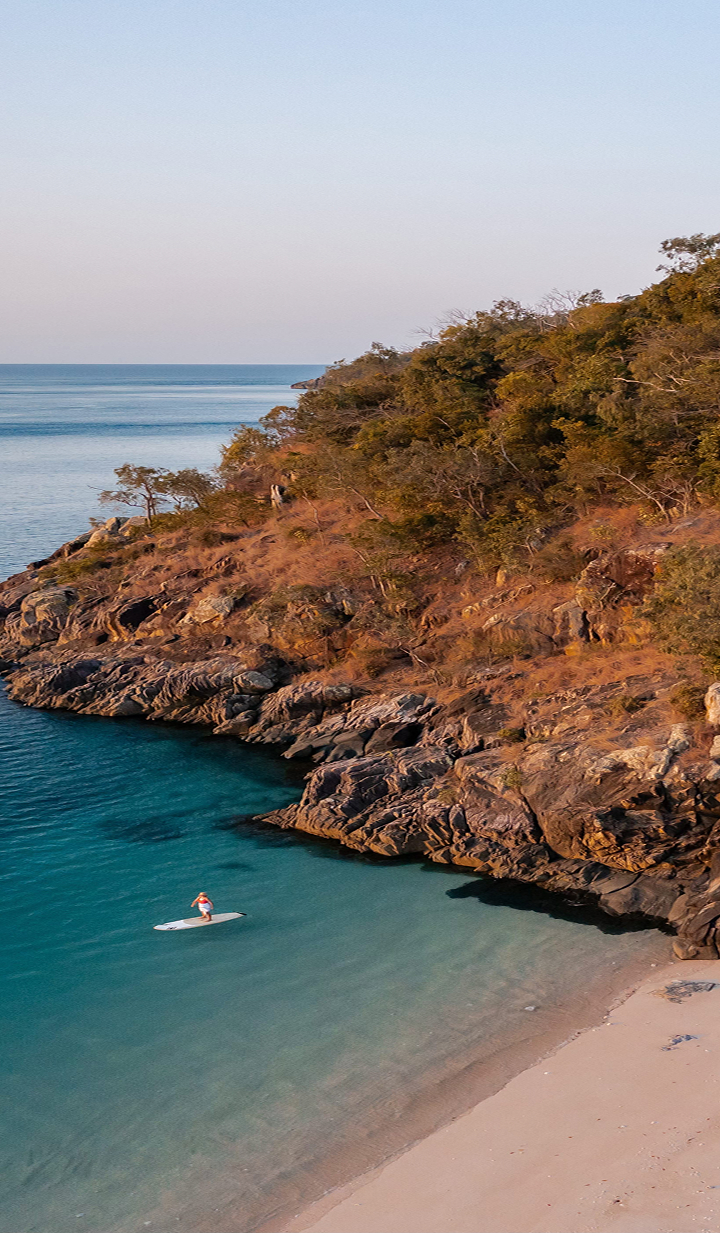 Woman paddleboarding in calm blue water near a rugged coastline