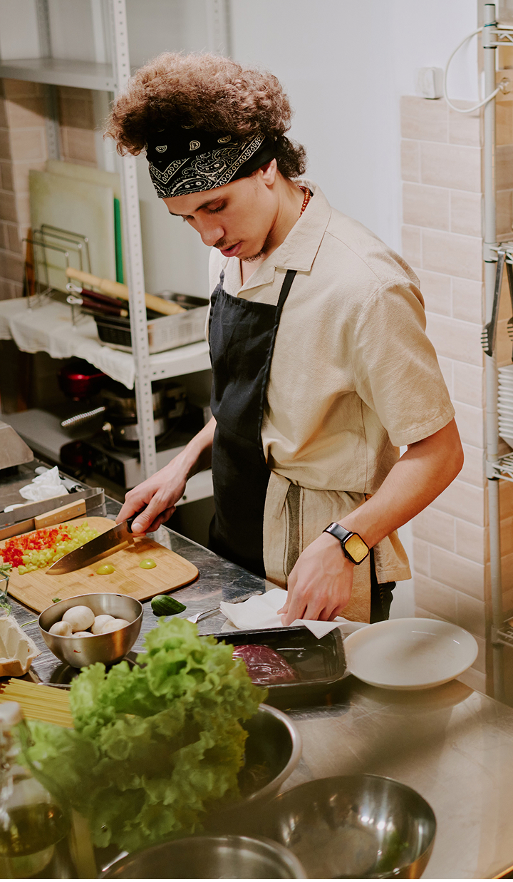 Young chef chopping vegetables at a stainless-steel bench