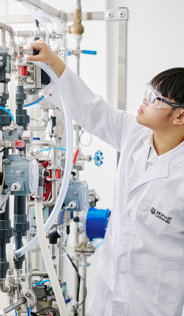 A Monash University student in a white coat learning how to operate a machine.