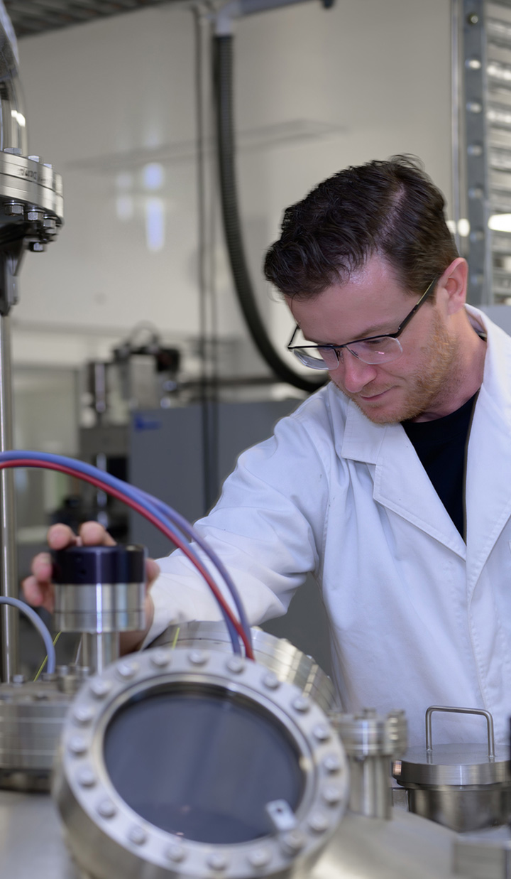 A man in a lab coat and glasses operating scientific equipment in a laboratory.