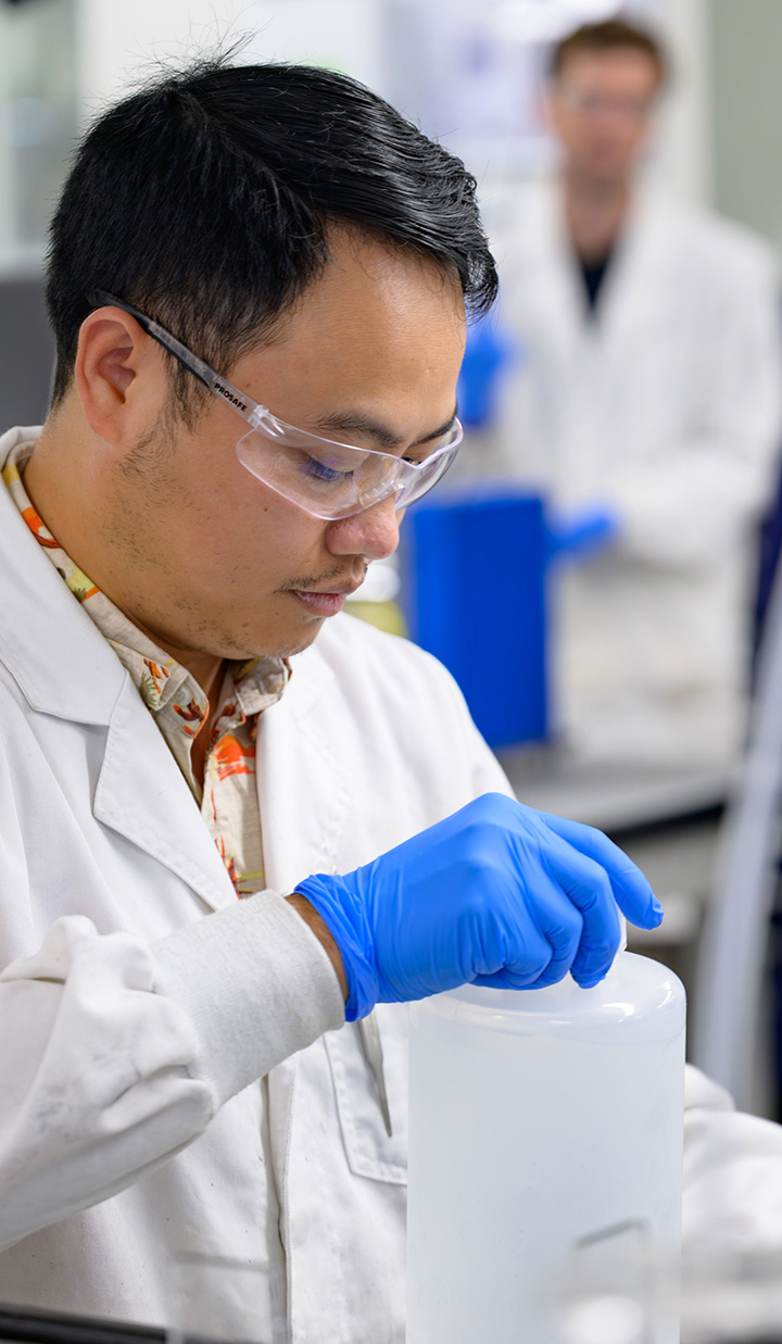 A man in a lab coat and gloves working with laboratory equipment.