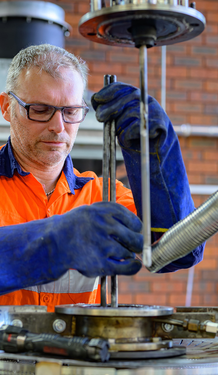 A man wearing PPE glasses and gloves operating a machine while holding two steel rods.