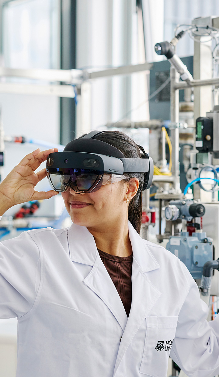 A woman in a lab coat wearing augmented reality glasses in a laboratory setting.